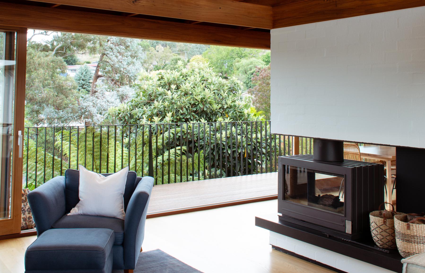 Living room, exposed timber structure and clad celling. open sliding door with treetops. integrated fireplace in brick 